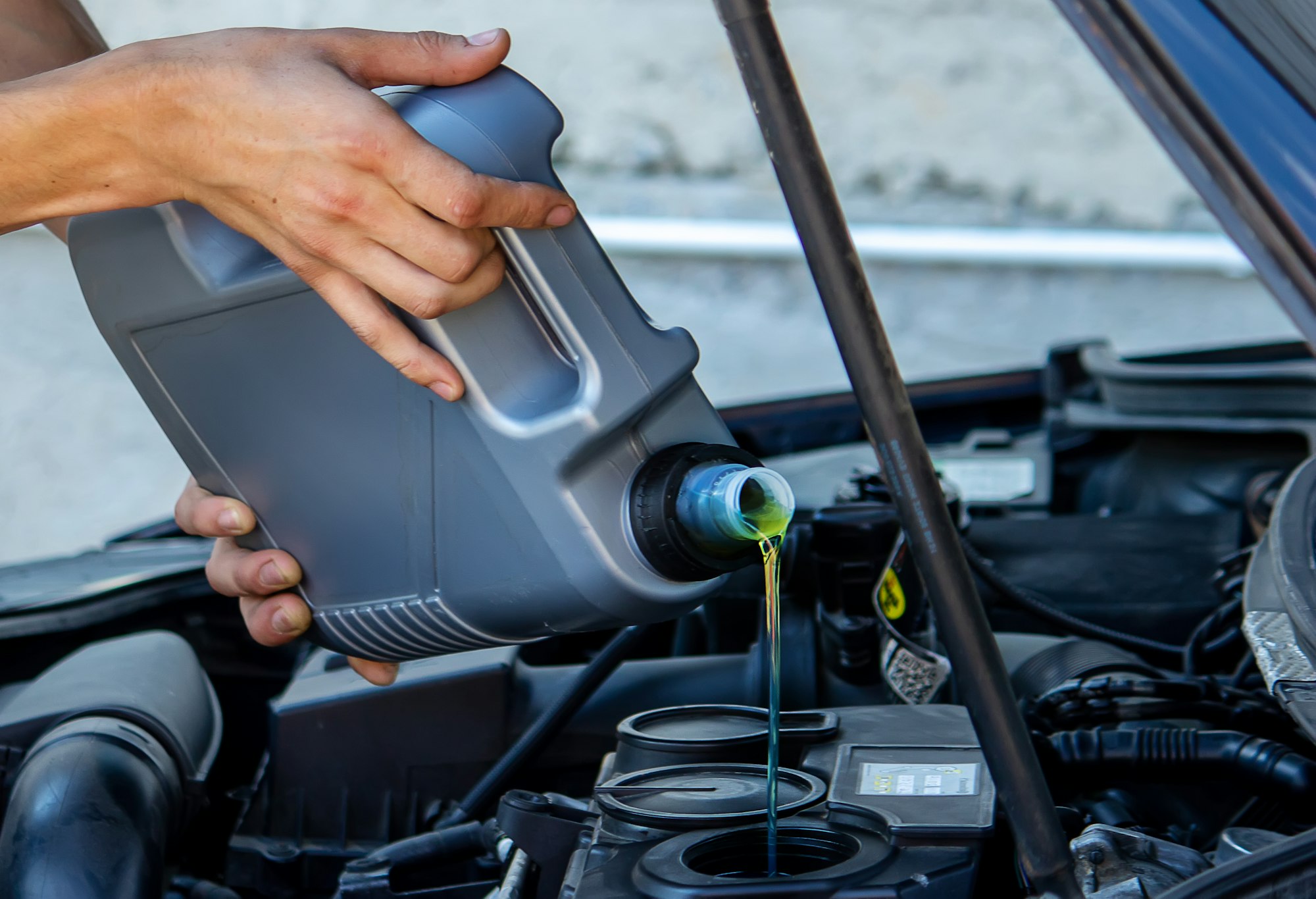 An auto mechanic changing oil pours oil into a car engine.