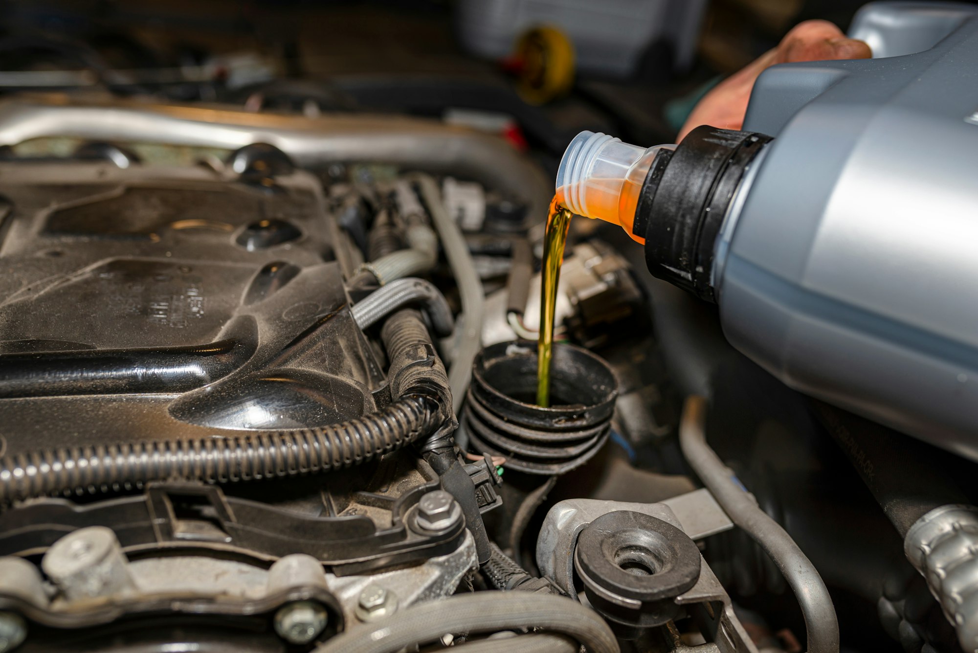 Car mechanic pours new car oil into the engine from a plastic tank in a car workshop.