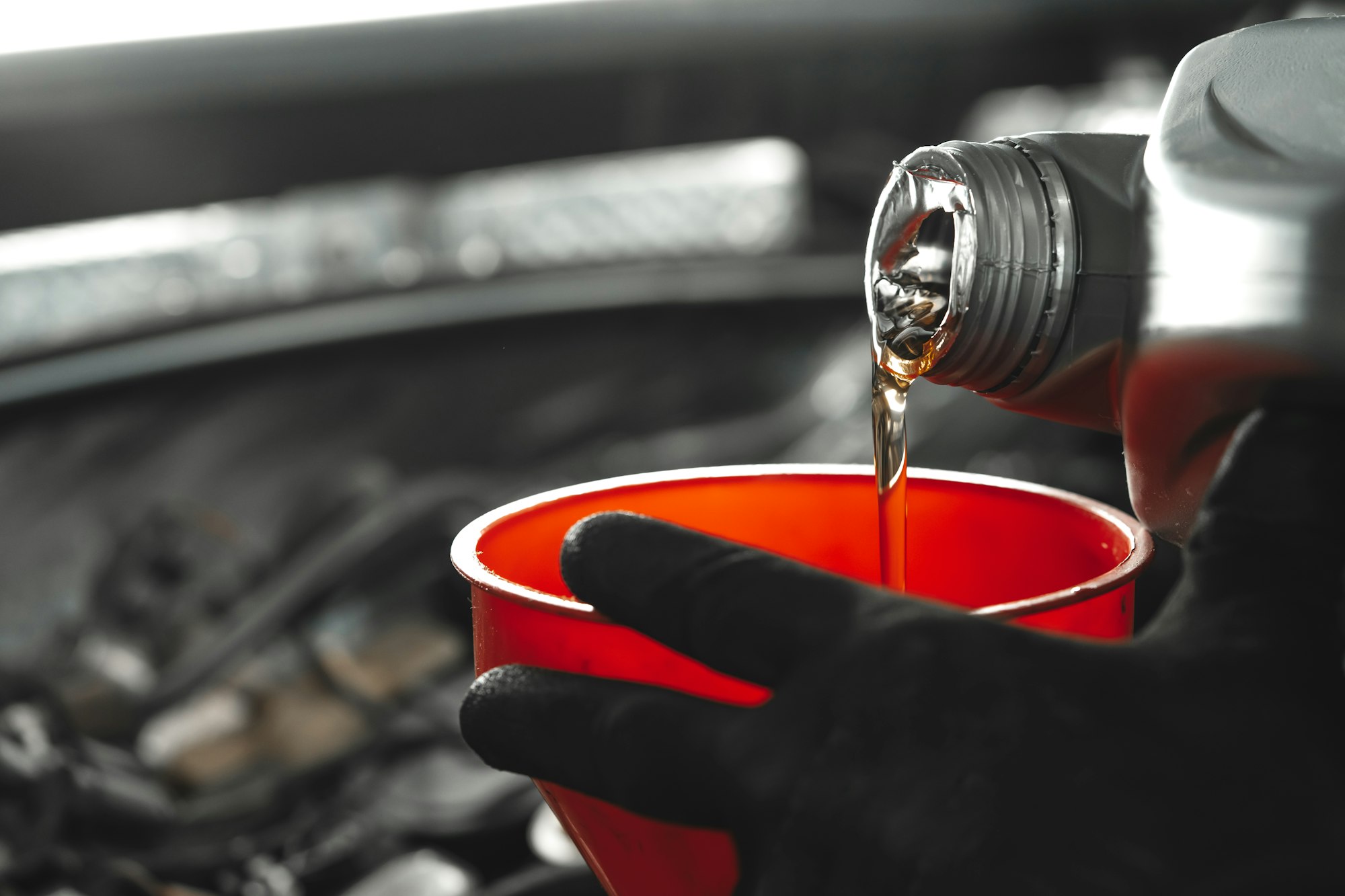 Close up of car service worker pouring new oil into car engine