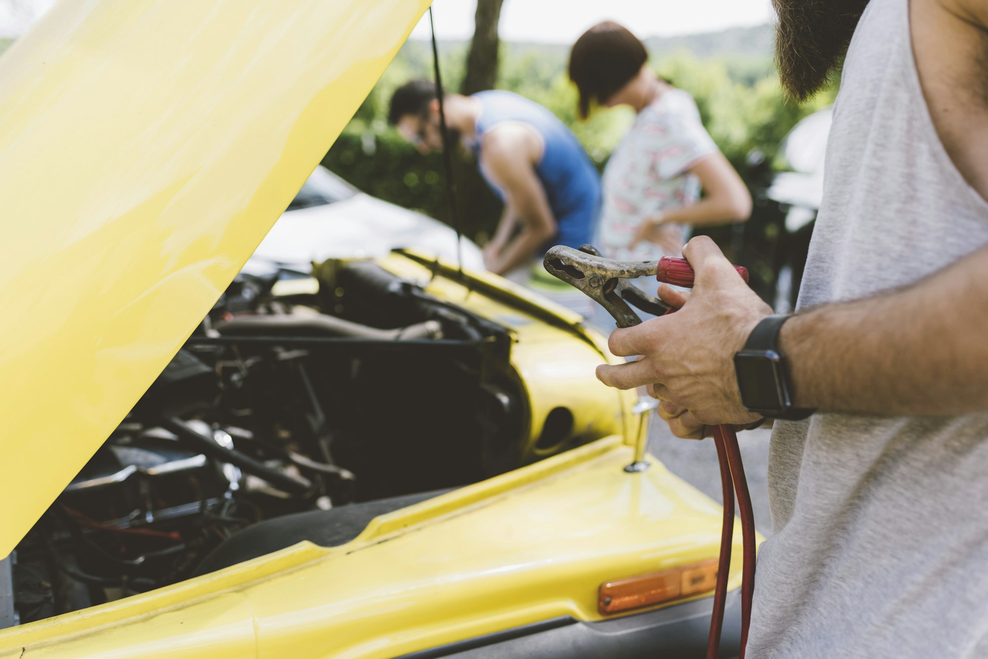 Young adults on road trip using jump leads to start vehicle