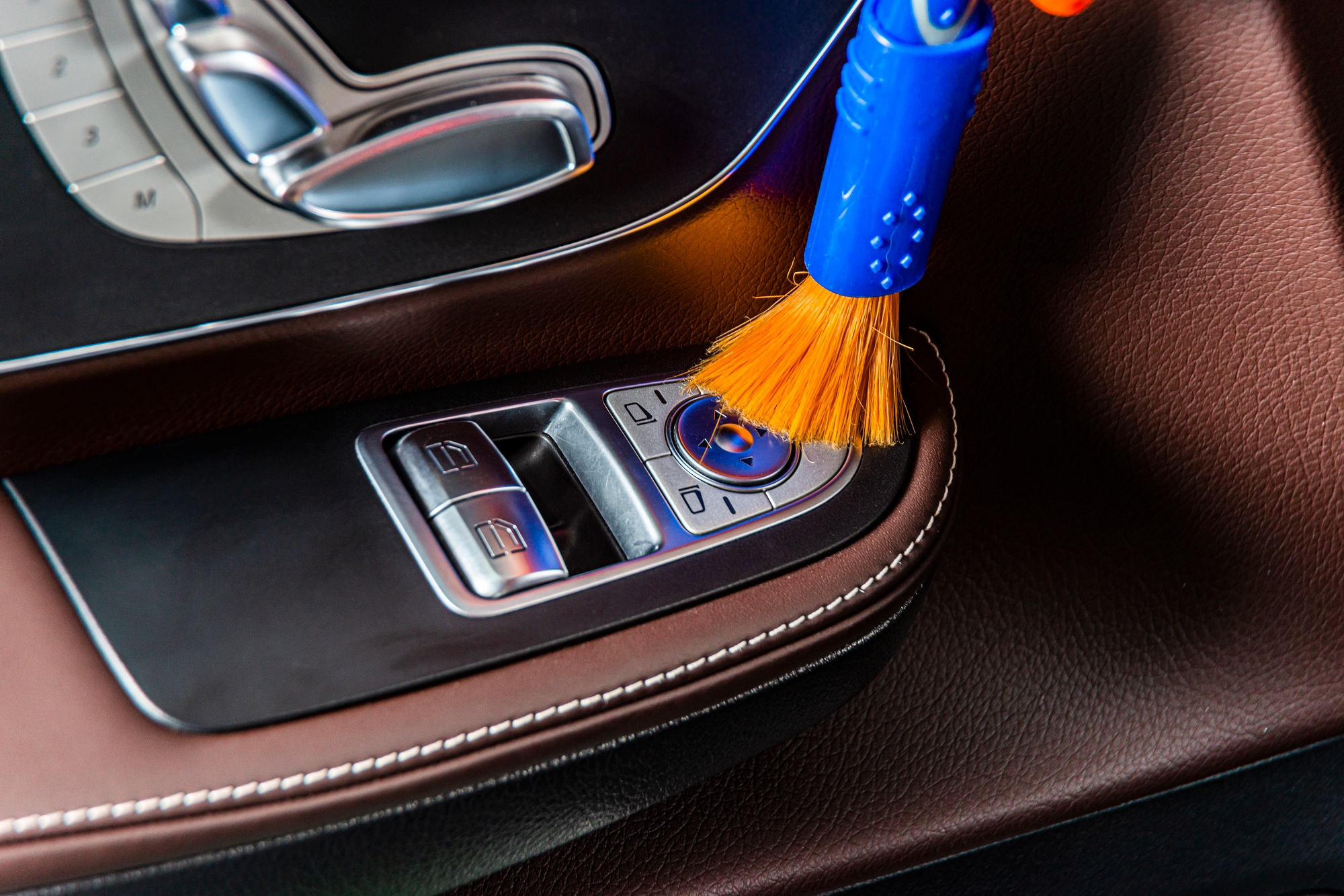 A man cleaning car interior panels and dashboard with a brush