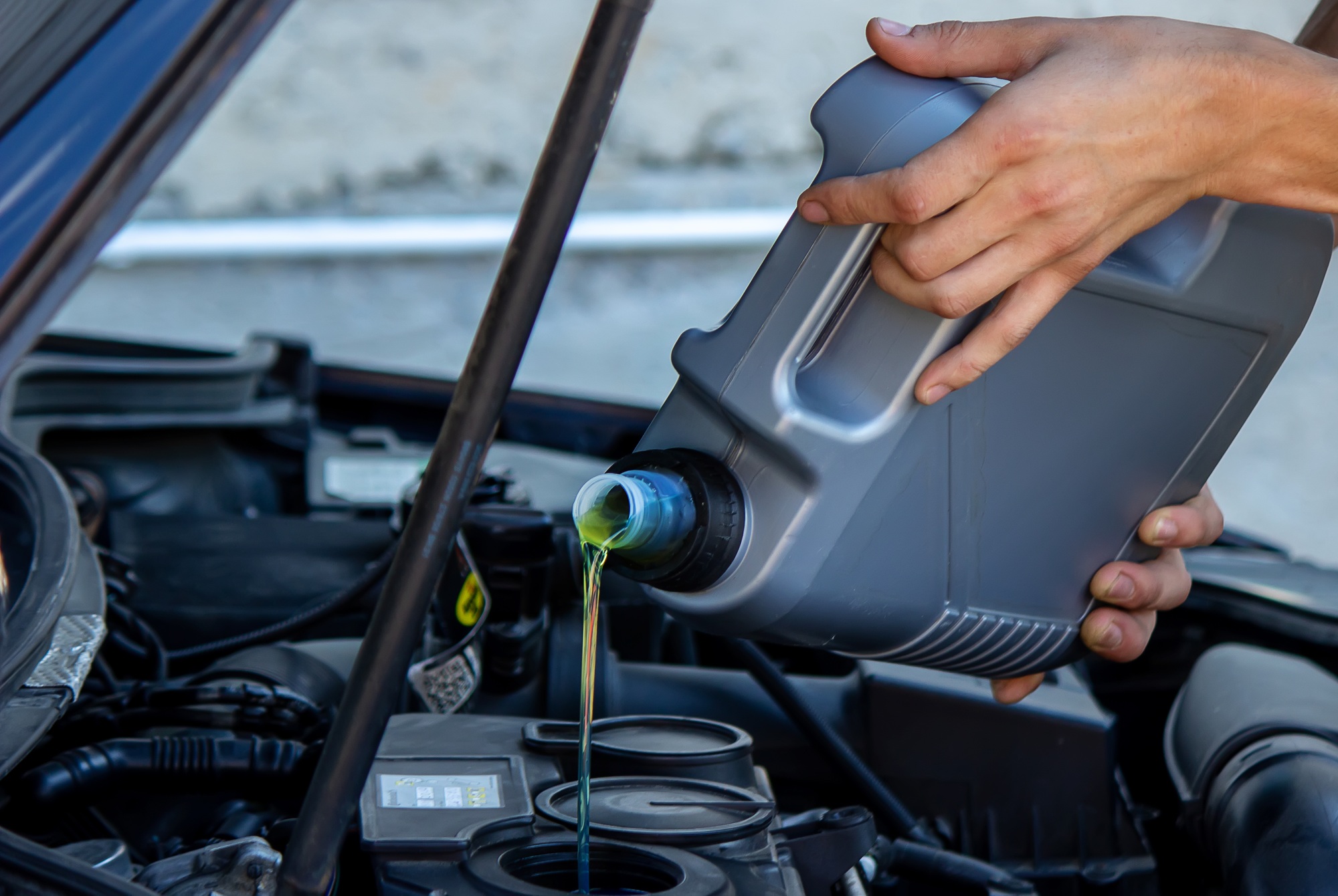 An auto mechanic changing oil pours oil into a car engine.