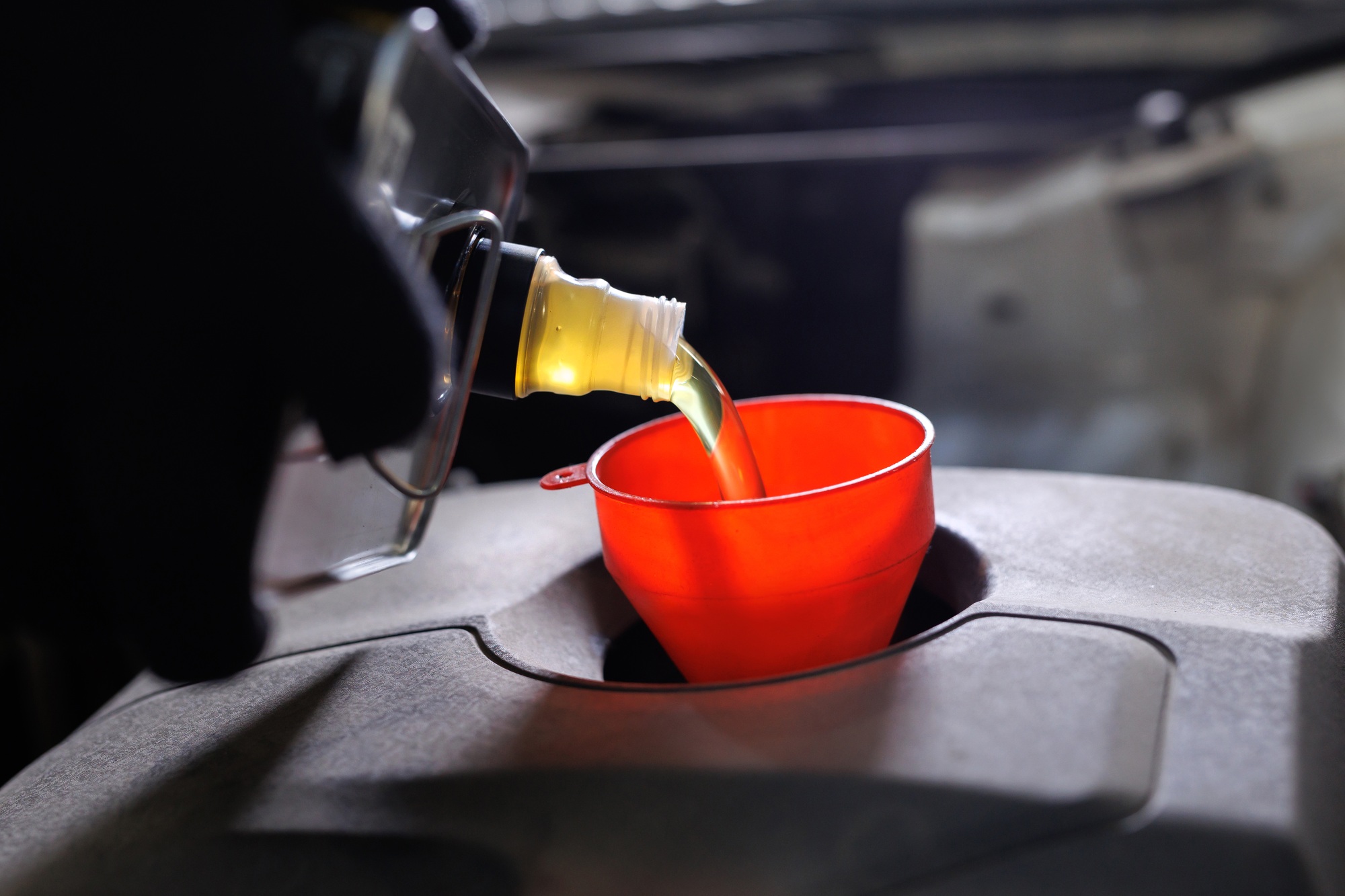 Car mechanic replacing and pouring fresh oil into engine at maintenance repair service station.