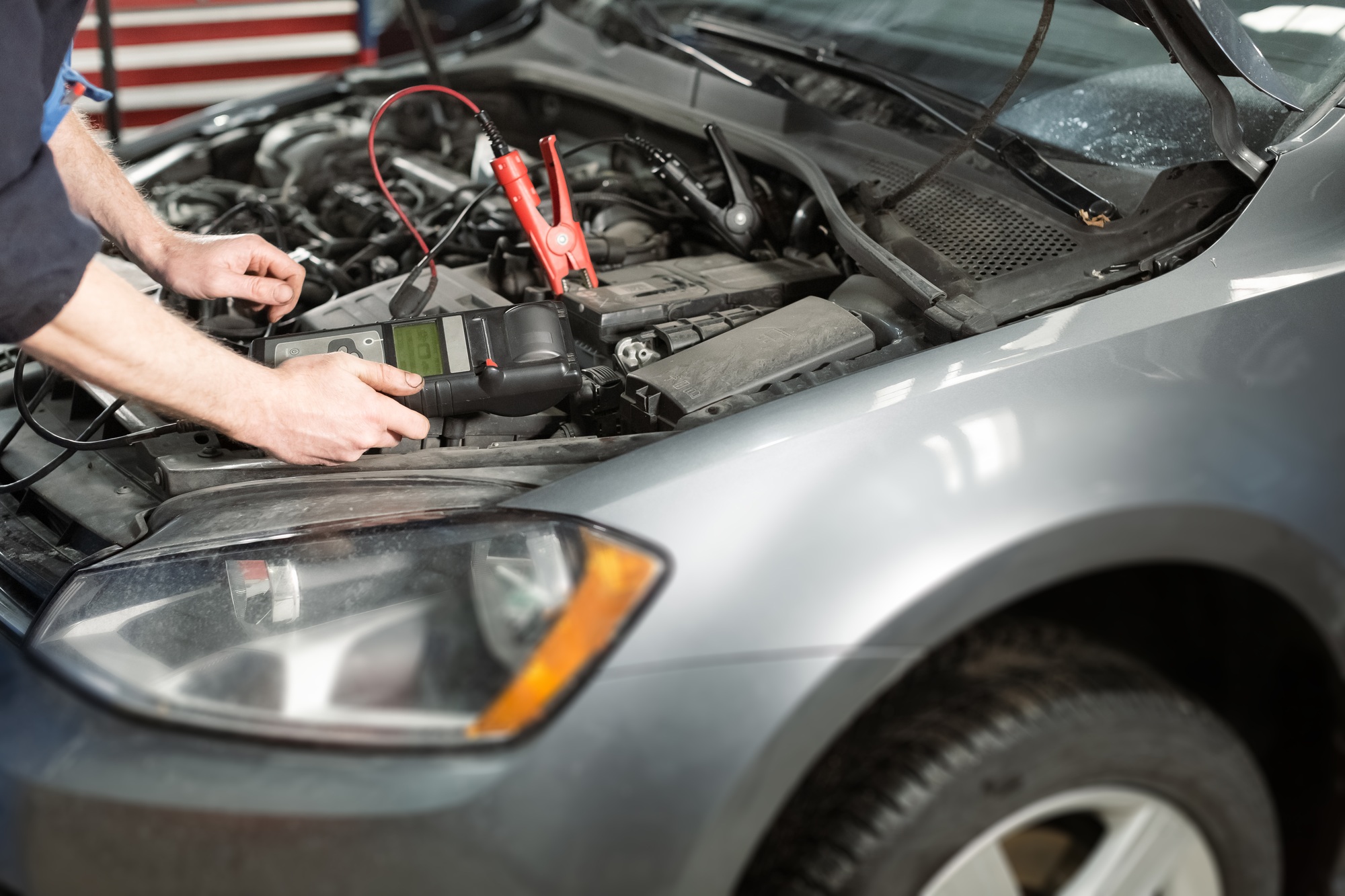 Male hands holding modern utility and checking voltage of automobile battery