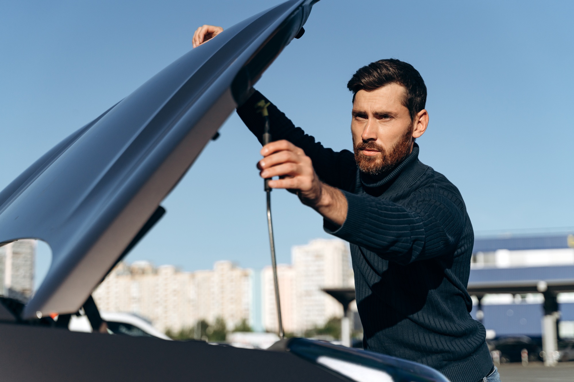 Young man looking under the hood of breakdown car. Car breakdown.