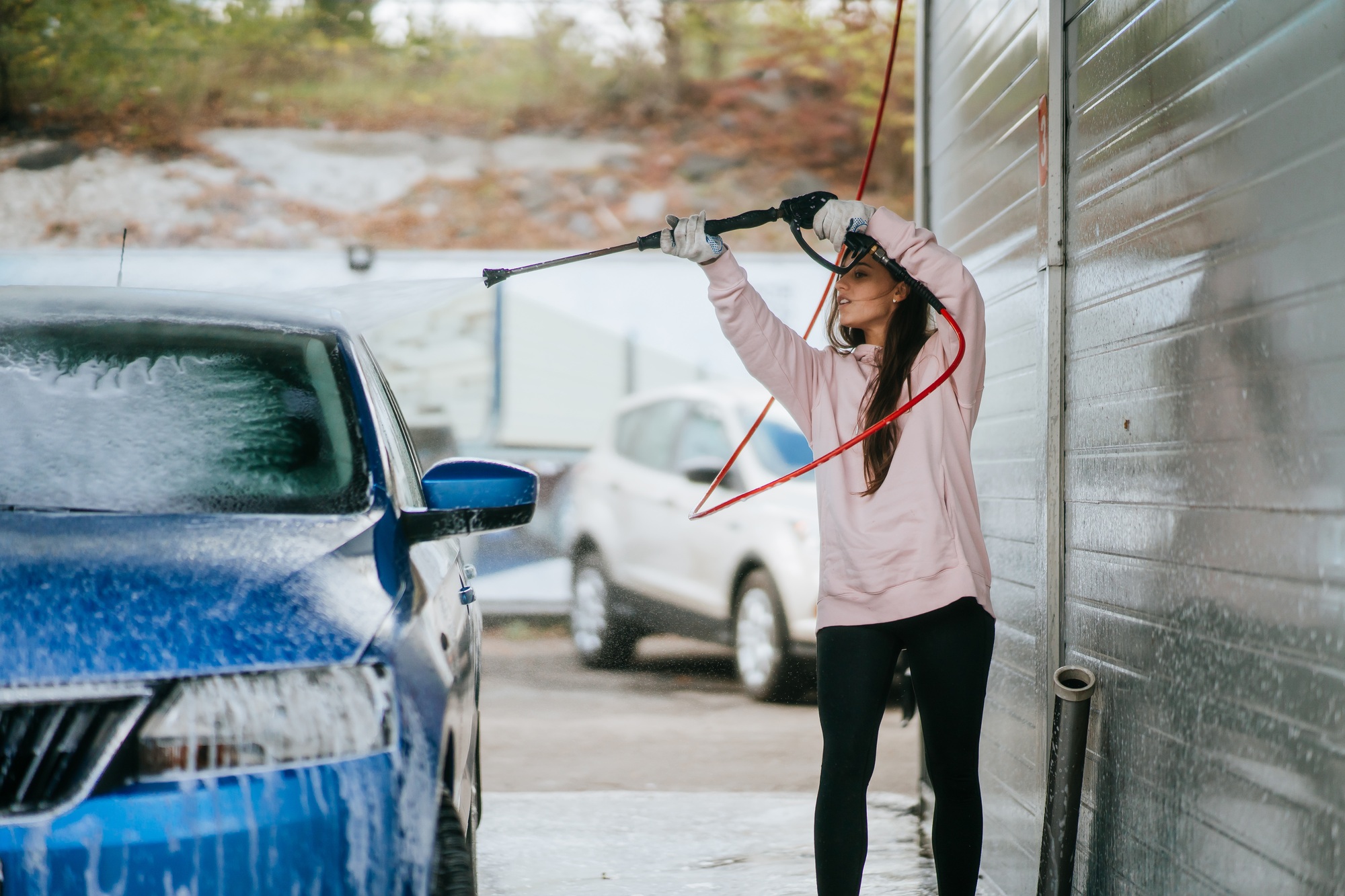 Young woman washing blue car at car wash