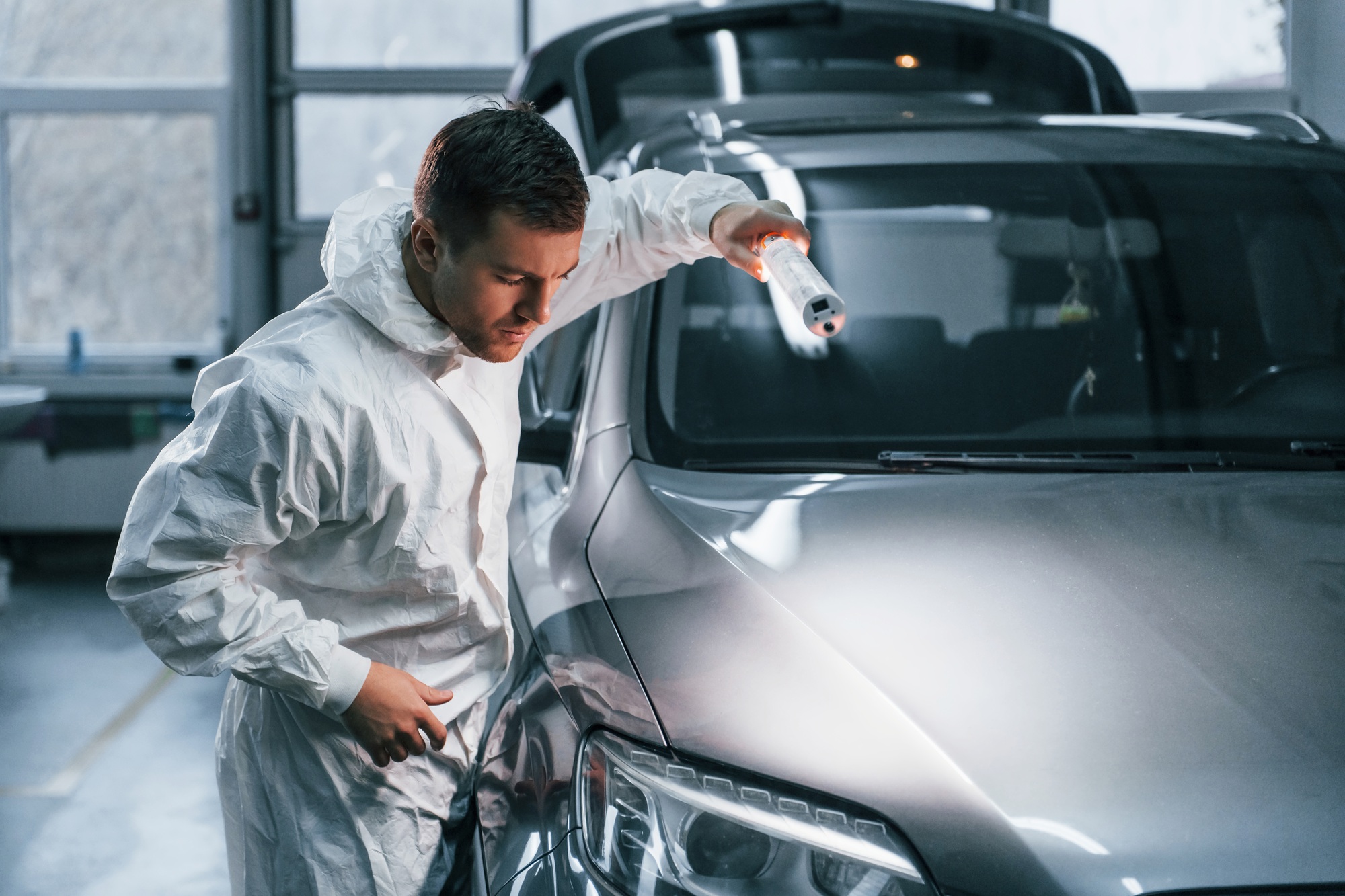 Silver colored car. Man in uniform is working in the auto service